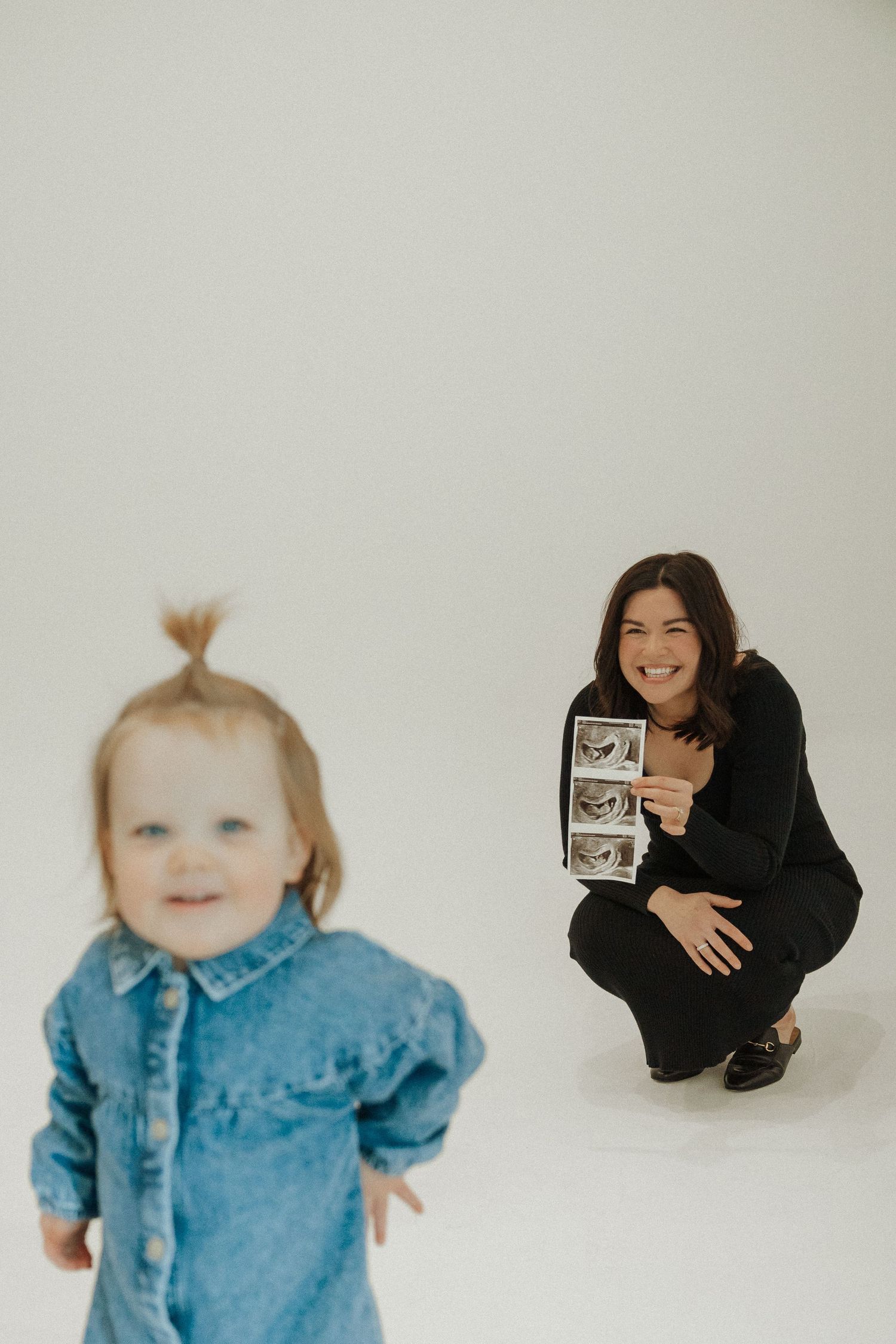 Studio portrait with toddler in denim and person showing ultrasound photos.