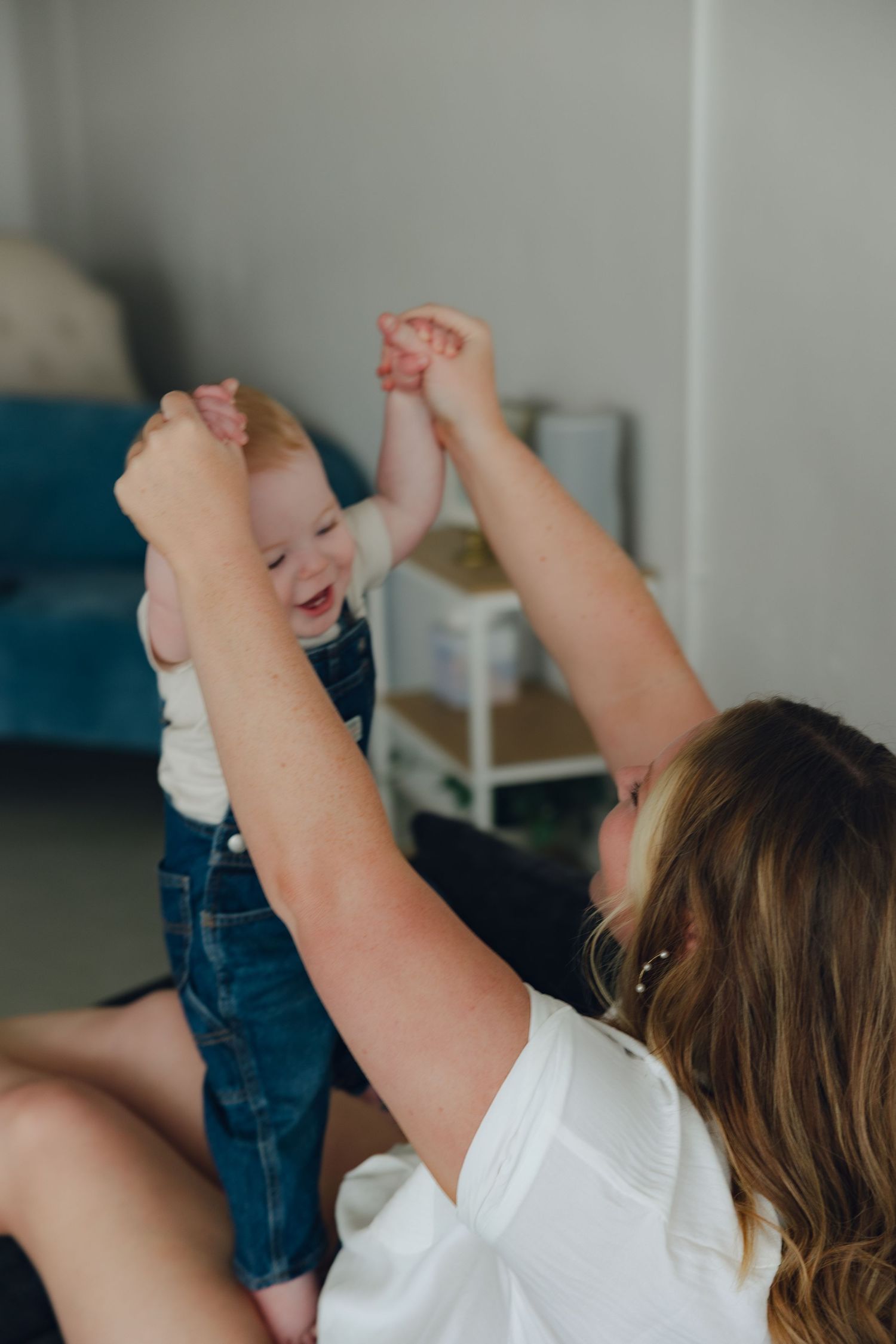 A heartwarming photo of a parent lifting and playing with a laughing baby wearing denim overalls.