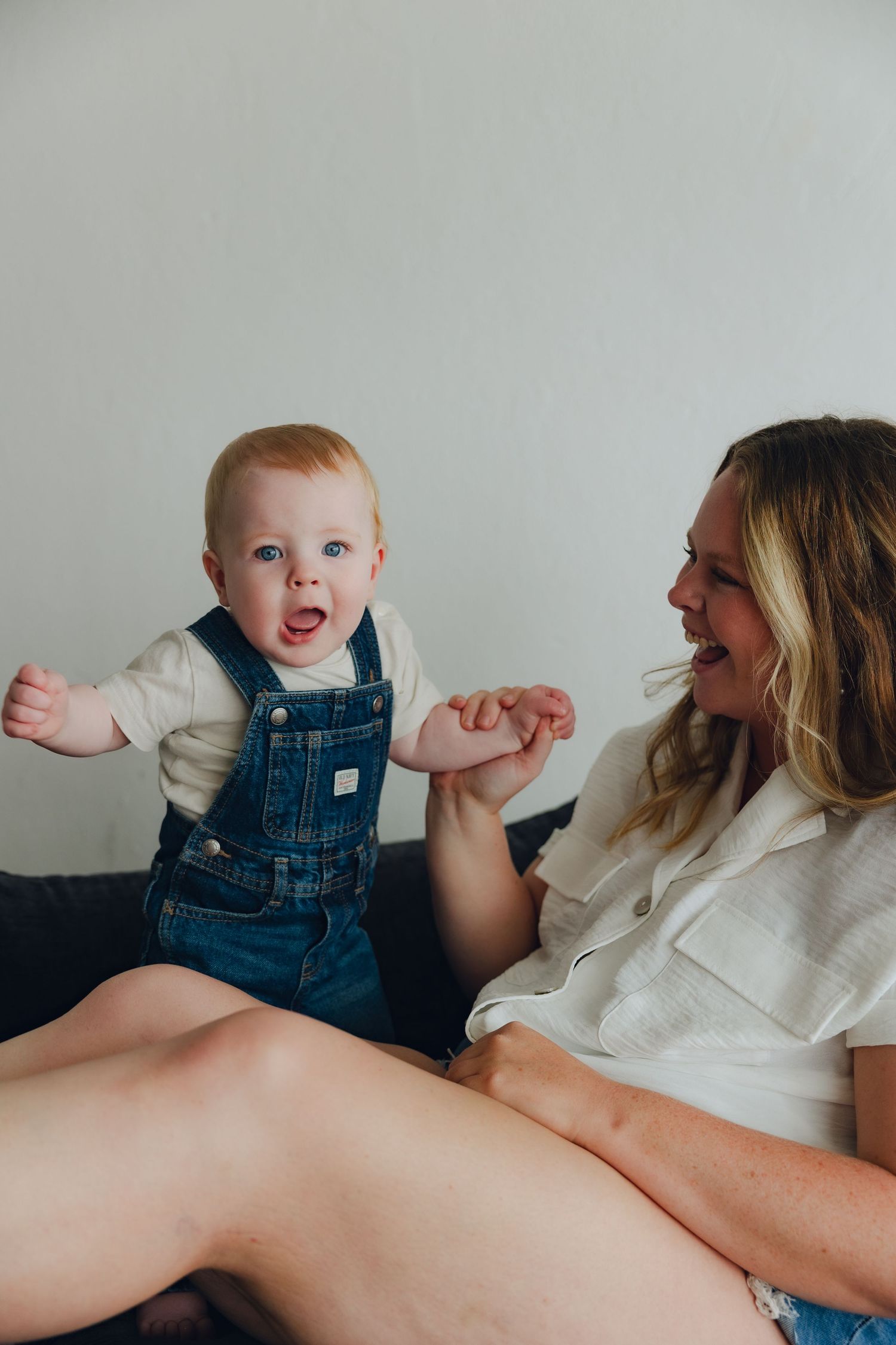 A joyful moment captured between parent and baby in denim overalls sitting on a couch together.