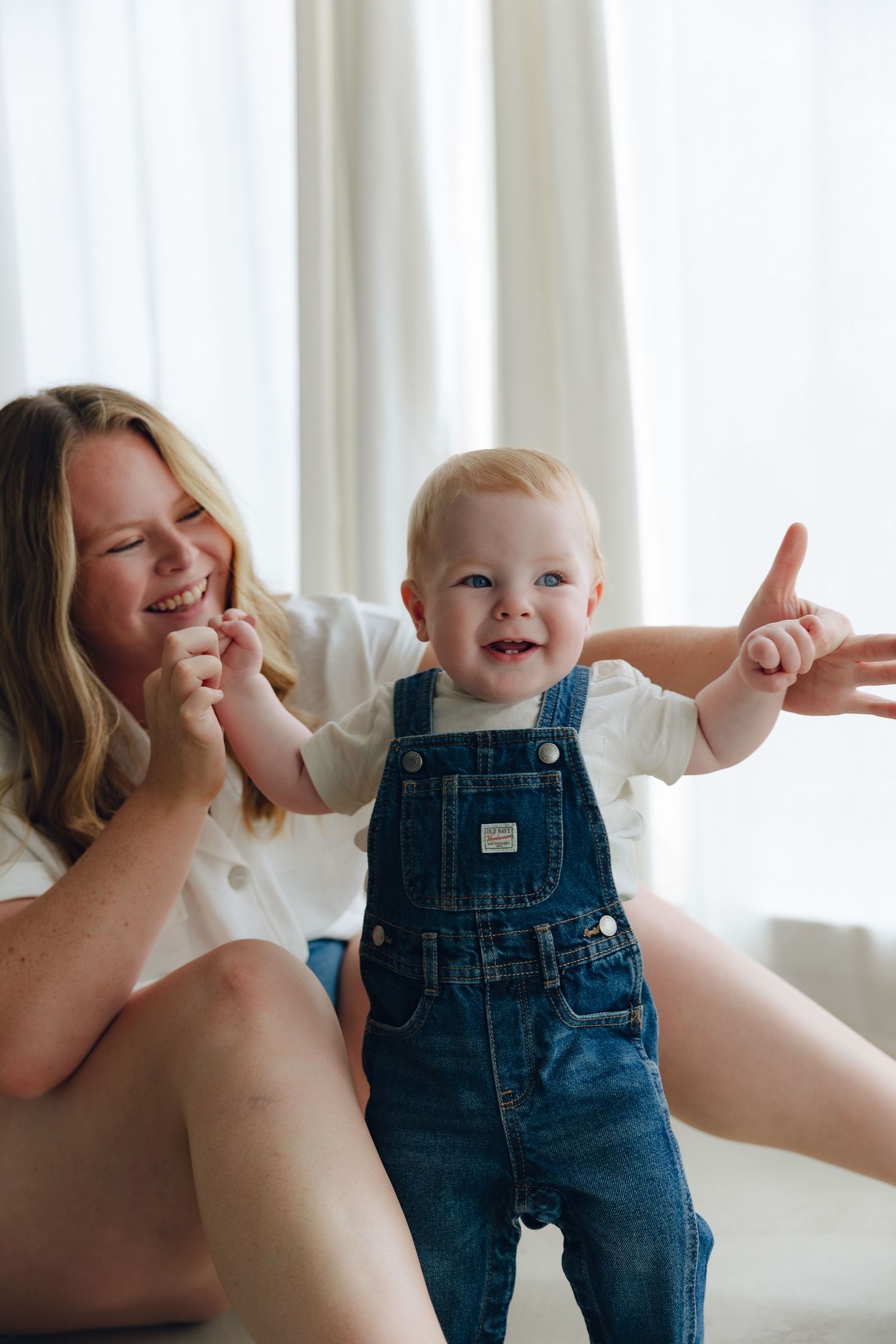 Joyful moment of laughter and play with baby in denim overalls spreading arms wide.