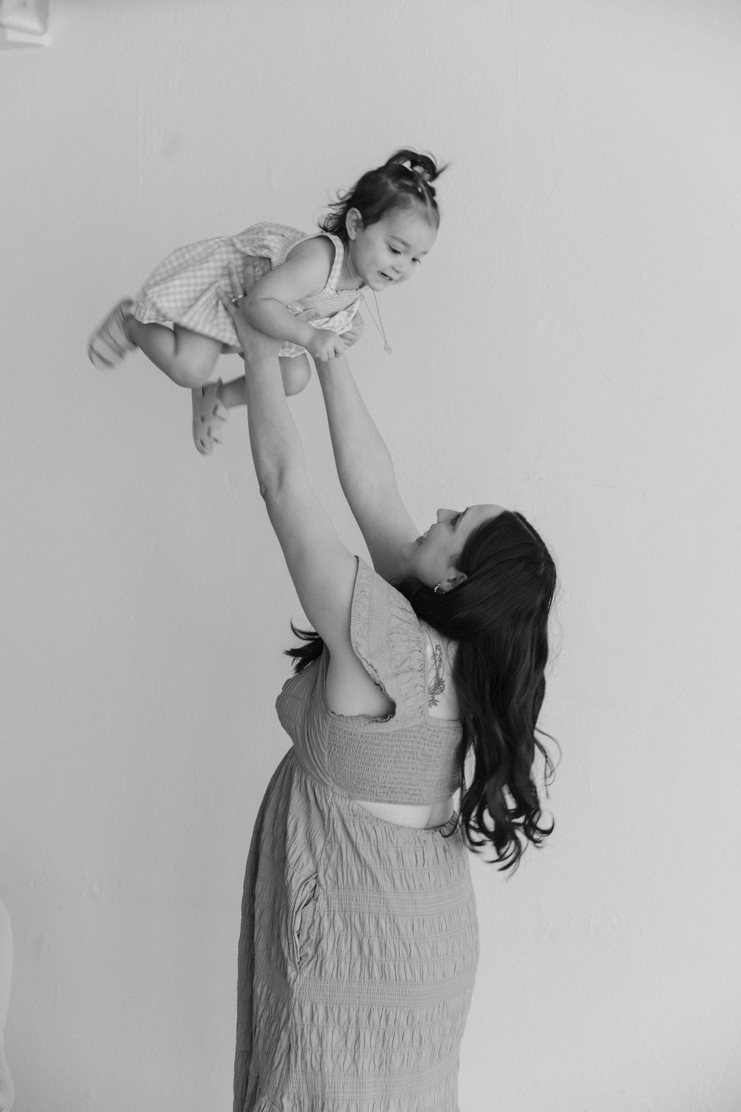 Black and white portrait of loving interaction between parent and child as parent lifts baby up high with joy.