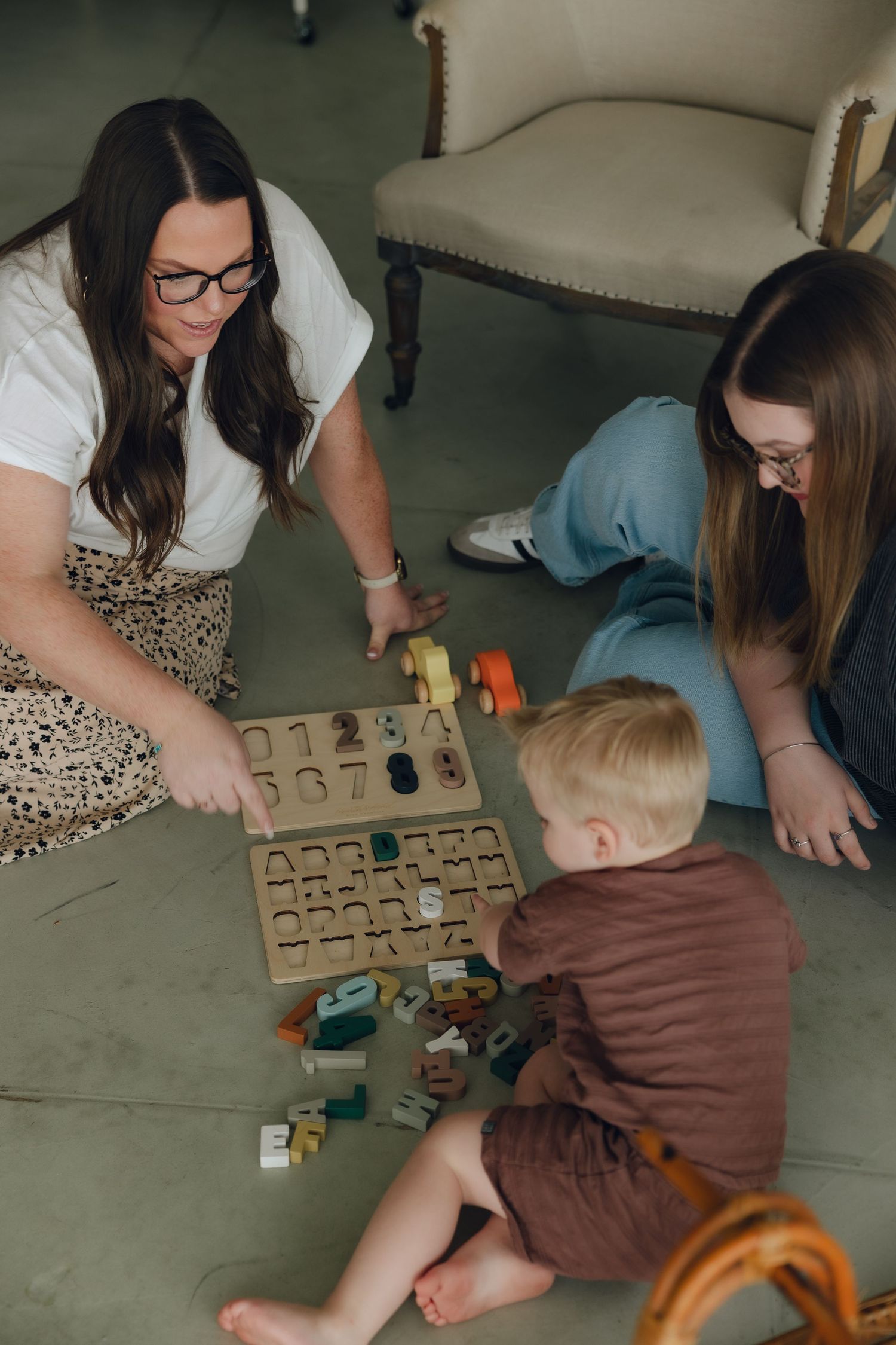 Group playing with educational wooden number blocks and toys on concrete floor during learning activity.