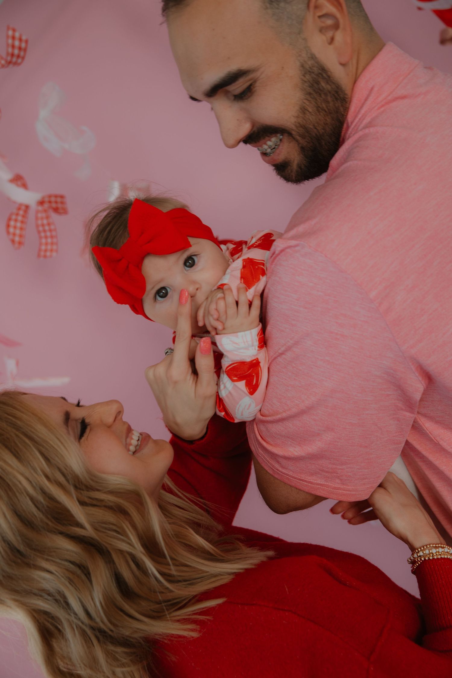 A sweet family portrait against a pink backdrop with Valentine's Day decorations.