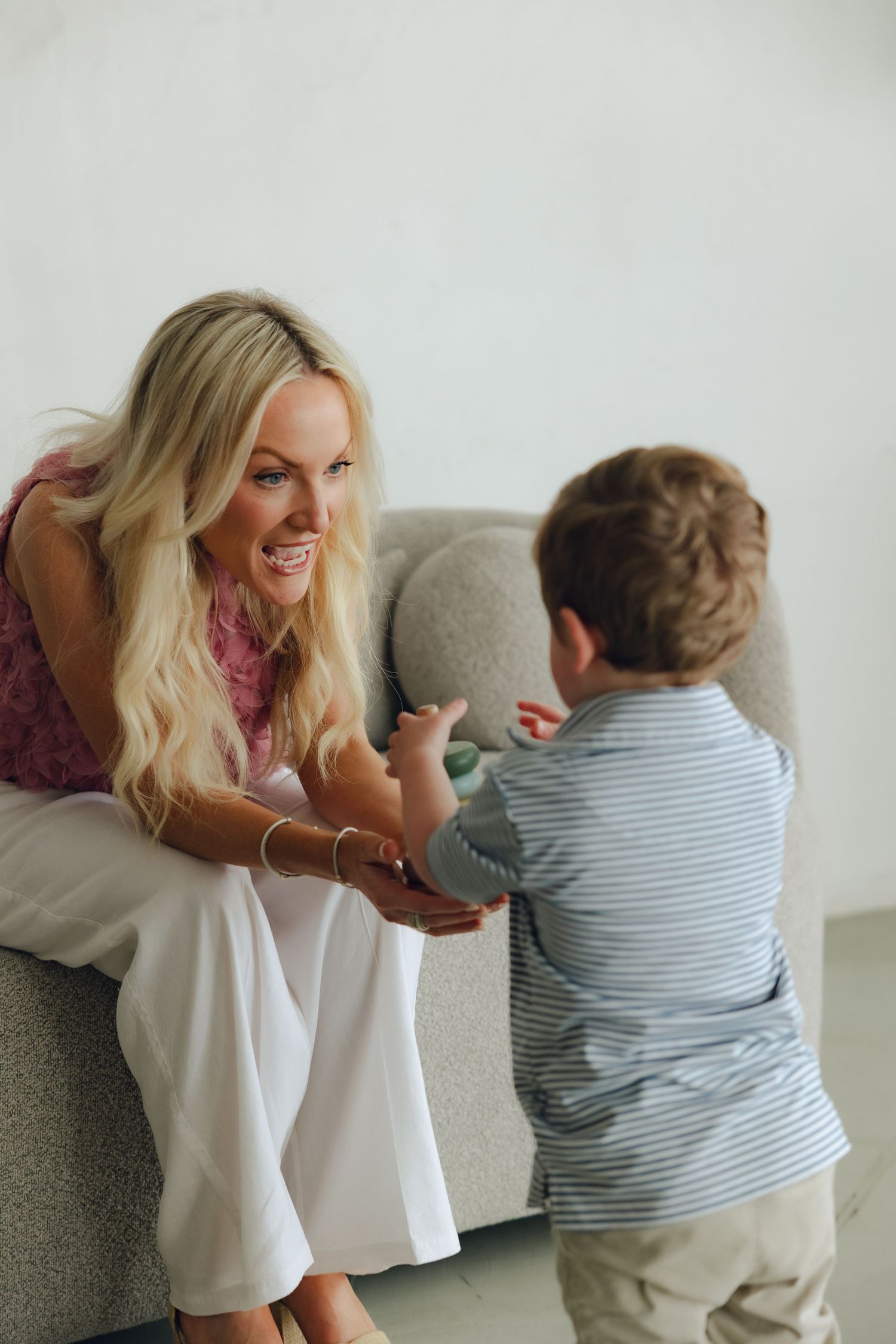 Joyful interaction on a gray couch as child in striped shirt engages in animated conversation indoors.