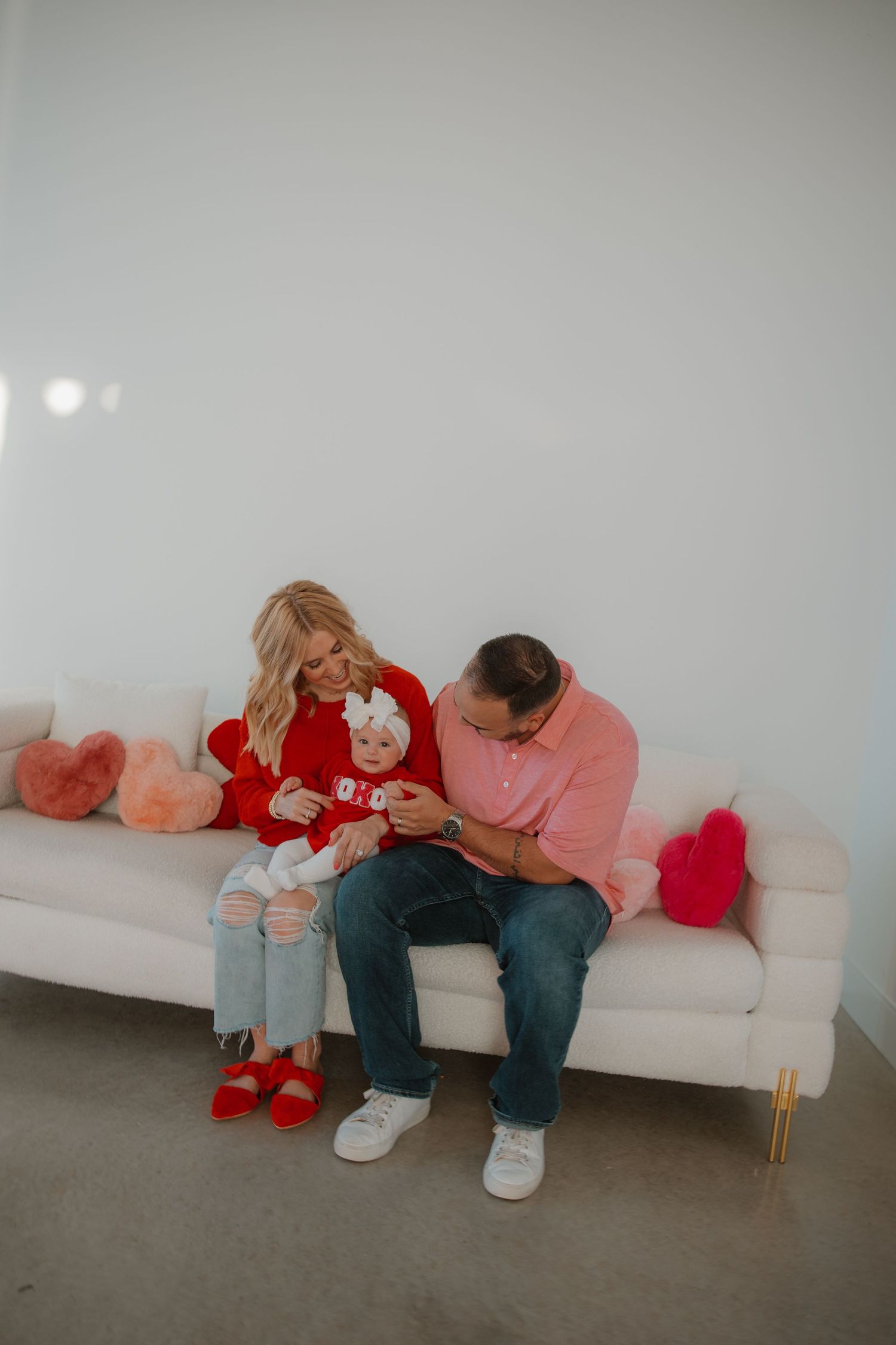 An intimate family moment on a white couch surrounded by heart-shaped pillows.