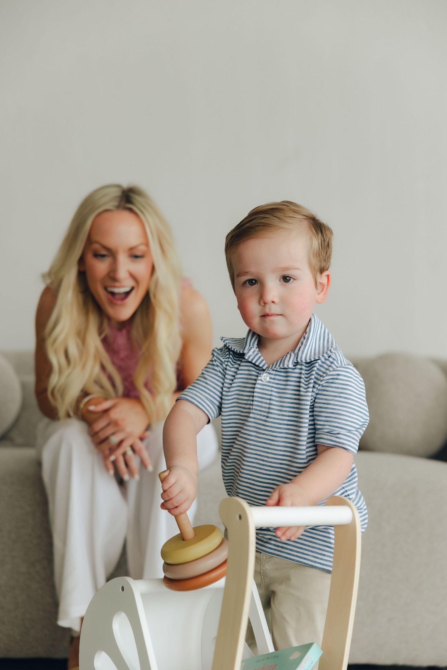 An excited parent watches a small child playing with a wooden kids' scooter toy at home.
