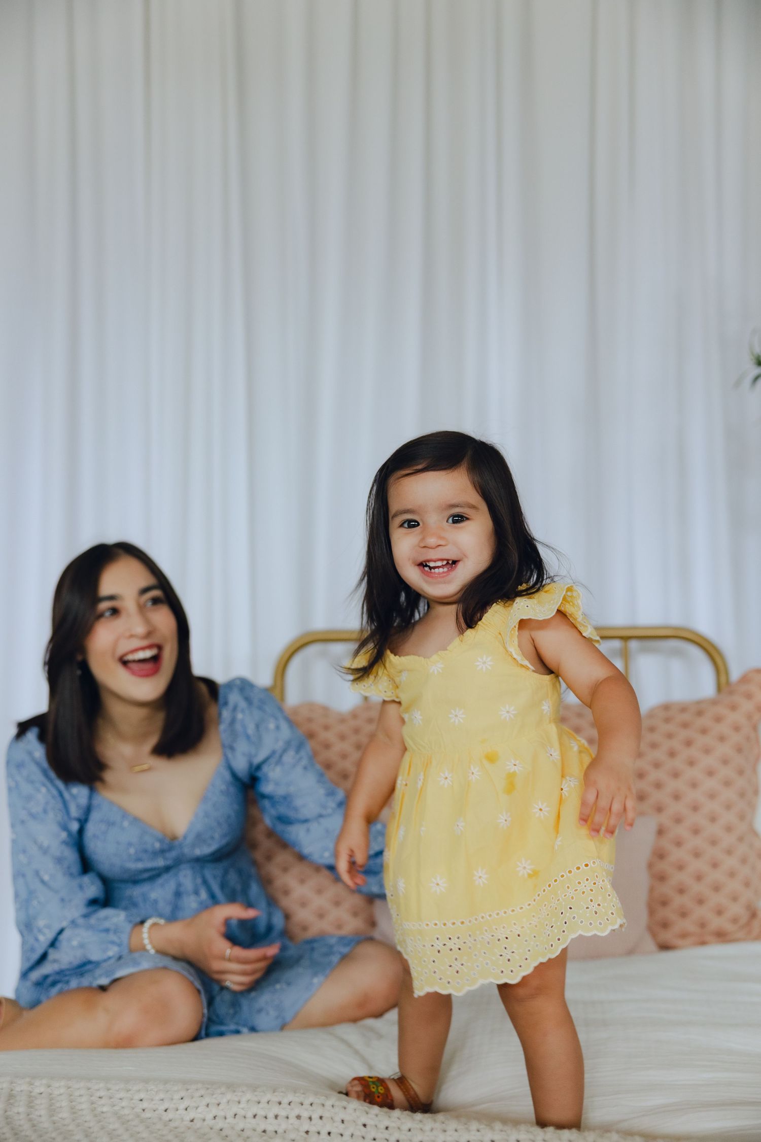 A happy moment shared on a white couch, with someone in a blue dress and a child wearing a yellow sundress.