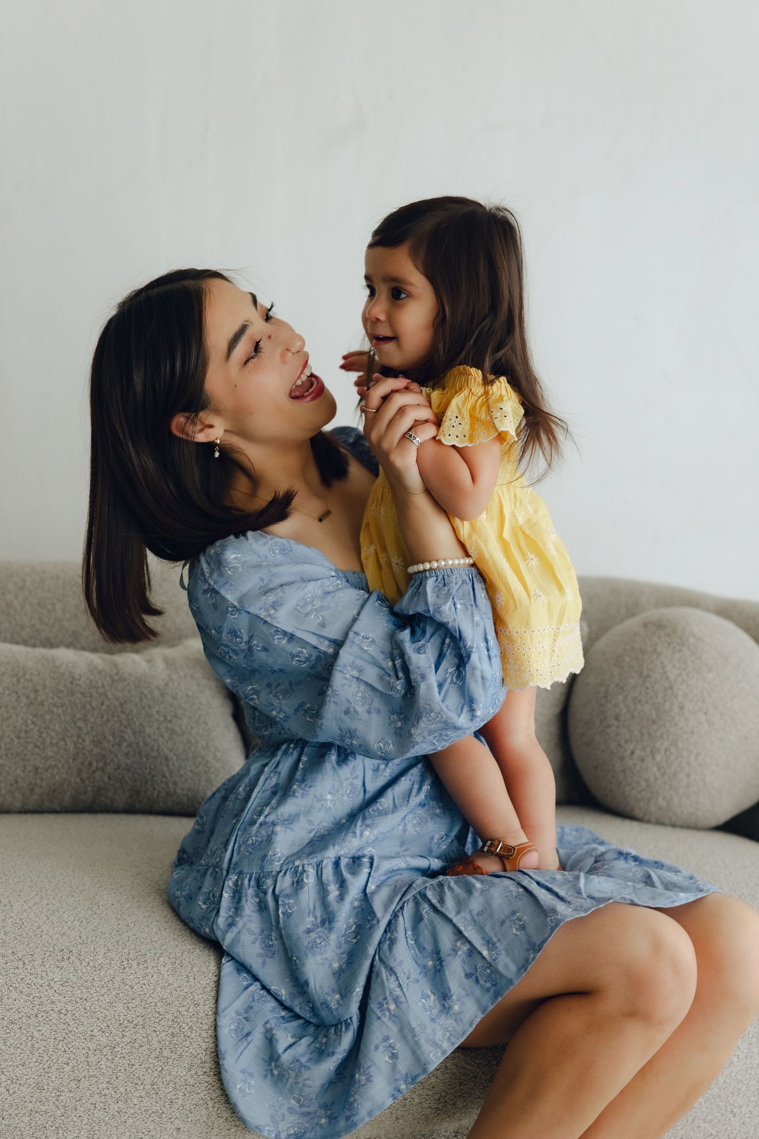 A playful moment shared between two generations wearing denim and yellow dresses while sitting on a gray sofa.