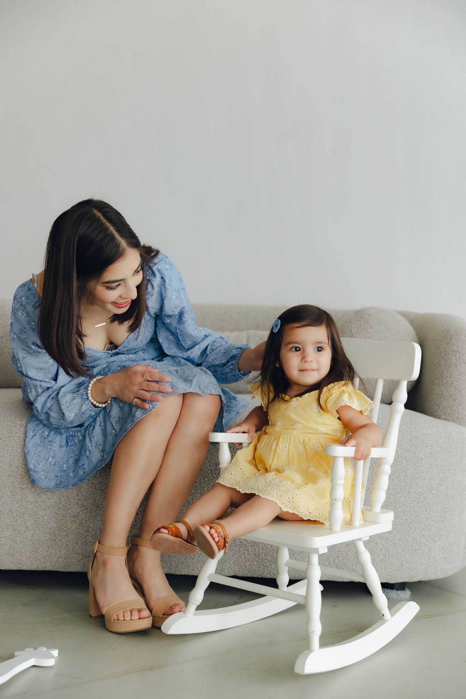 A parent and child sharing a tender moment on a cozy white rocking chair next to a gray sofa.