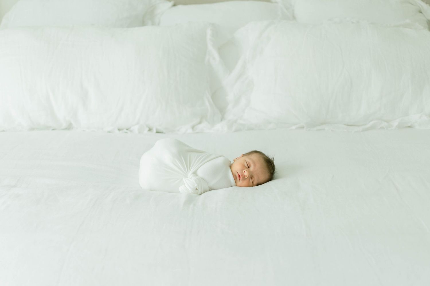 Peaceful newborn baby sleeping on white bedding.