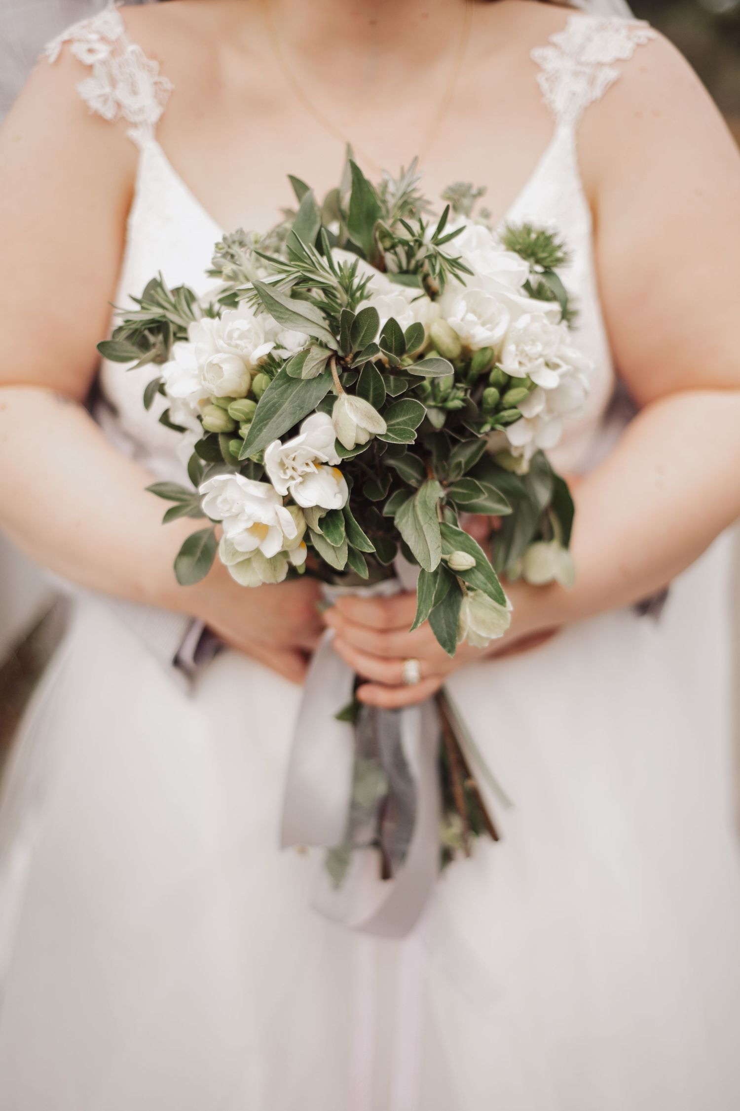 Close up of white and green wedding bouquet held by bride in lace dress.