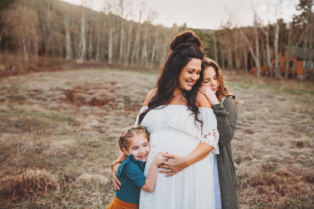 Pregnant woman and two daughters hugging and smiling with mountains in the background