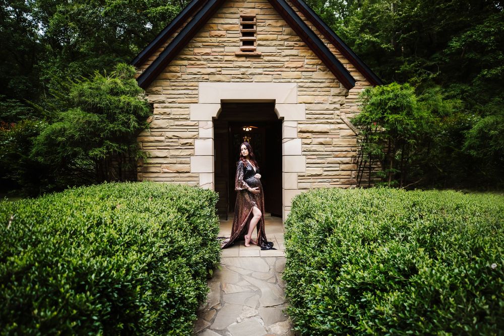Pregnant woman poses in front of building with trees and shrubbery for her maternity session in Dickson, TN