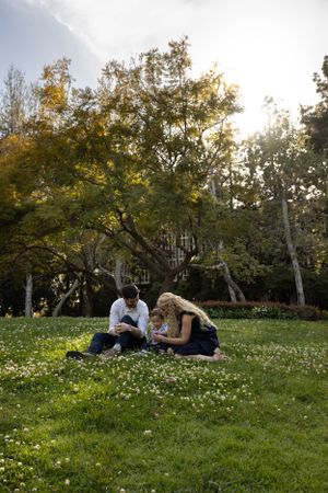 A family sits in a grassy field picking clovers.
