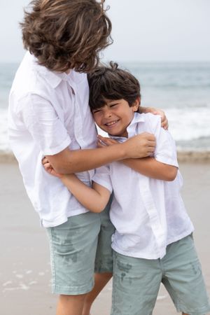 A candid portrait of two young brothers hugging while playing on the beach.