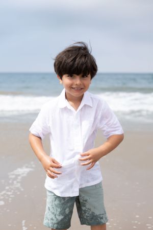 A young boy smiles and laughs while showing his shirt and shorts have been splashed by the waves on the beach.
