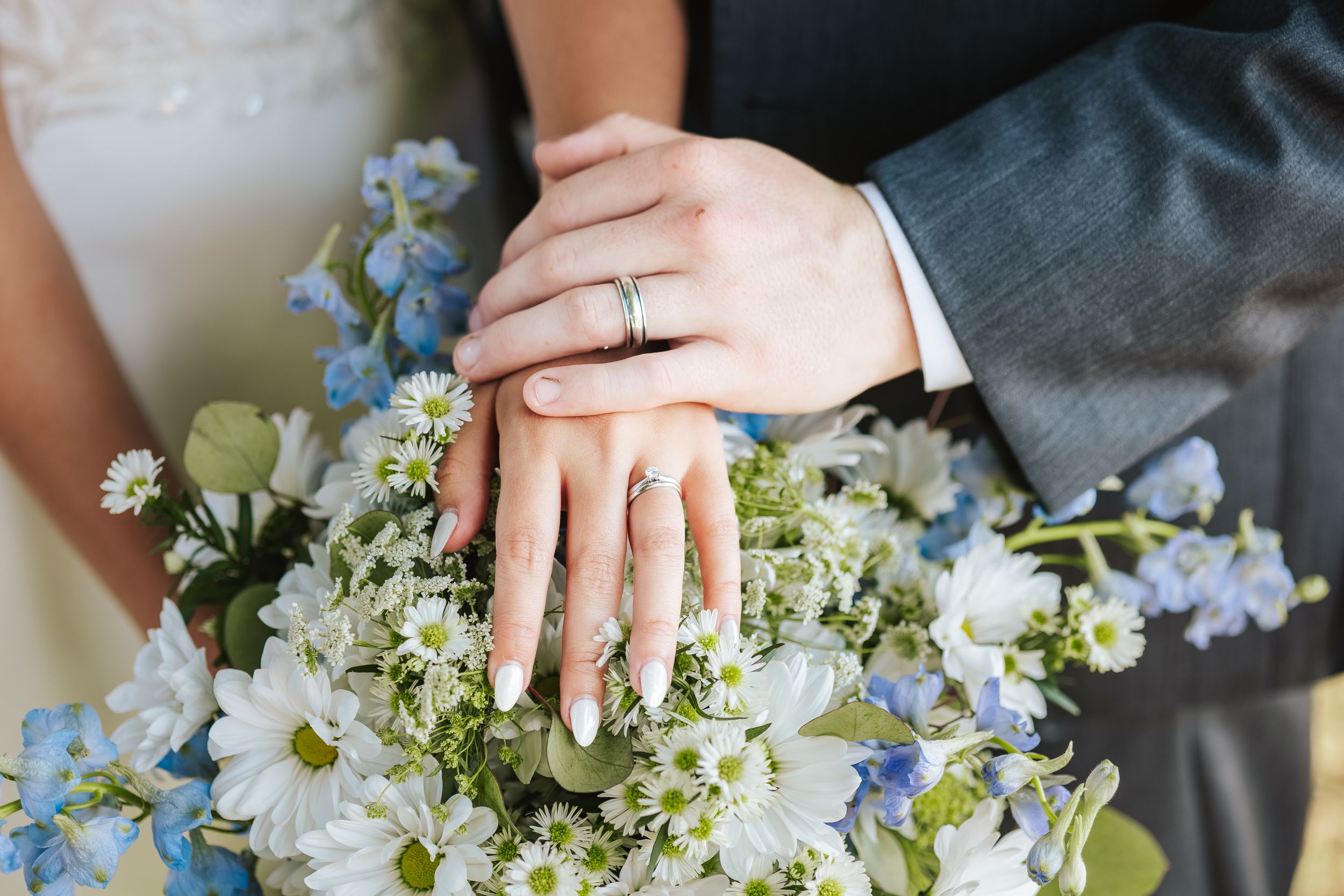 Wedding detail shot showing rings and floral arrangements with blue and white blooms.