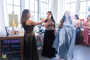 Women browsing vendor booths at an indoor market or craft fair with bright natural lighting.