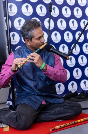 Musician playing traditional flute instrument against blue and white patterned backdrop.