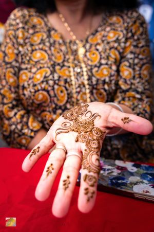 Intricate henna design decorates a hand wearing a traditional patterned orange and black outfit.
