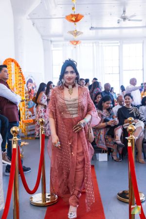 Attendee wearing a coral embroidered traditional outfit walks on red carpet at cultural festival event.