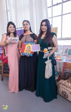 Three attendees displaying books and merchandise at literary event vendor booth.