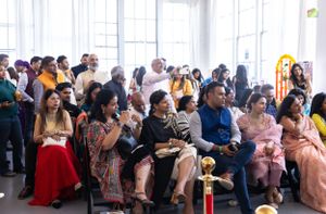 Large audience seated watching cultural performance in bright indoor venue.
