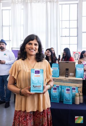 An author displays their book 'Kaveri' with teal product boxes arranged on a table in the background.
