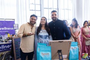 Three people pose together at a wellness event with blue product bags on display.