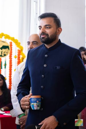 A speaker in a navy blue formal jacket holds a cup during a cultural event.