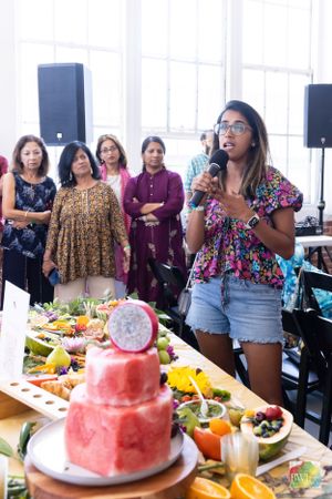 A speaker presents near a colorful fruit platter and pink watermelon cake display.