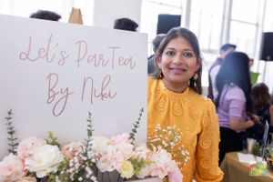 A tea party display with pink flowers and handwritten sign in a bright indoor setting.