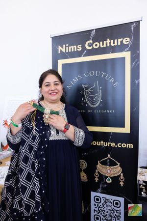 A jewelry vendor displaying elegant pieces in front of Nims Couture branded banner.