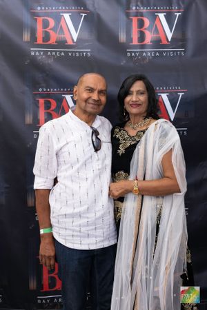 A couple in traditional Indian attire posing against BAV event backdrop.
