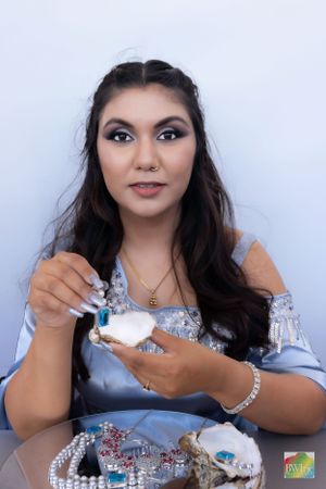 Woman in light blue dress showcases jewelry while holding decorative items.