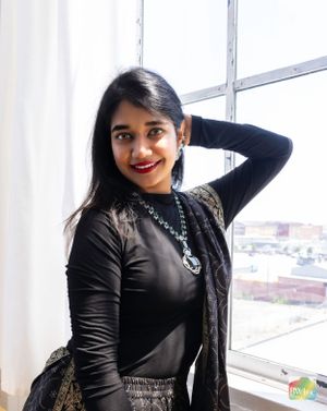 Woman in black outfit poses by window wearing statement necklace.