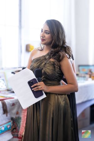 Woman in elegant bronze one-shoulder gown holds phone and documents at an event.