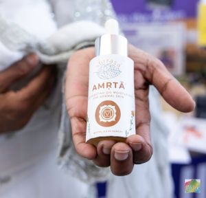 Close-up of hands holding Amrta branded white cosmetic product bottle.