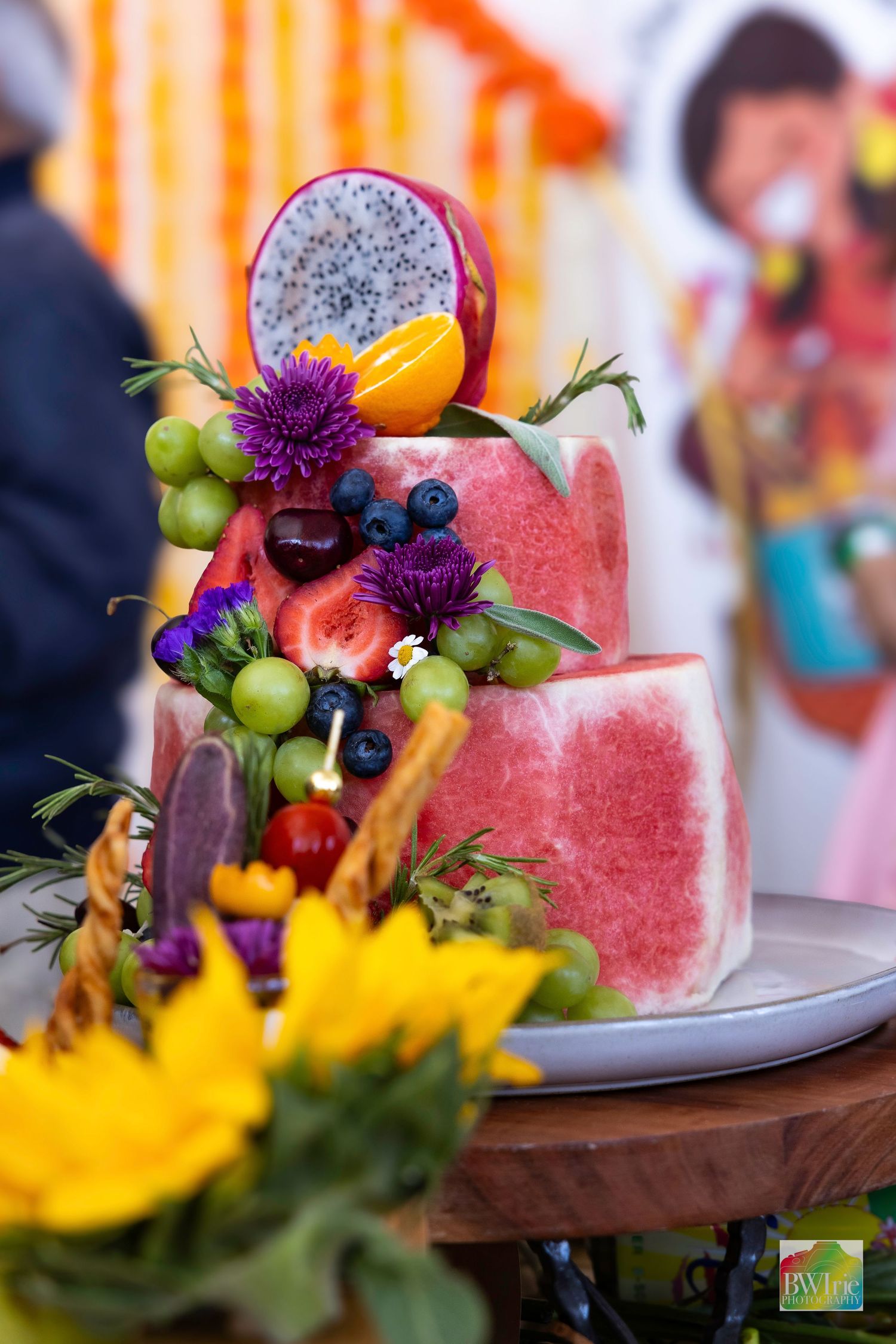 Beautifully arranged fruit platter with watermelon, grapes, berries and purple flowers decorated on a wooden surface.