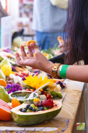 Close up of hands preparing fresh fruit in a halved watermelon bowl with colorful garnishes.