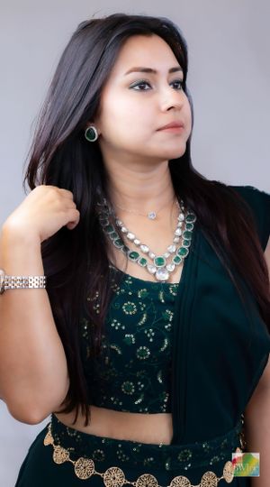 Woman in traditional dark green outfit adorned with matching emerald and silver jewelry.