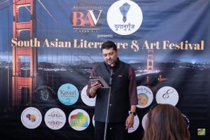Presenter addressing audience at Bay Area cultural festival with branded backdrop.