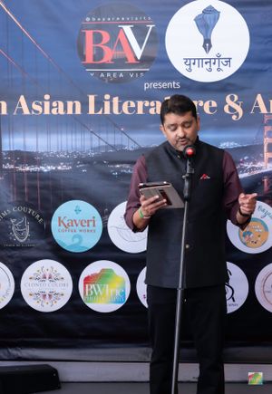 Speaker in formal black attire reading from phone at South Asian literature festival.