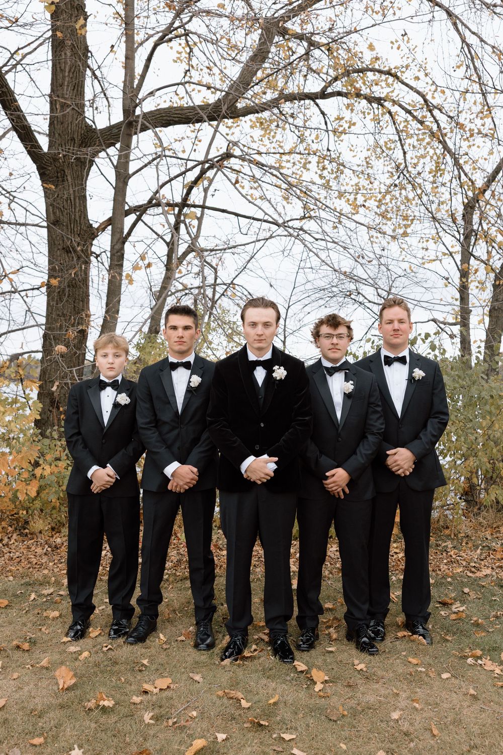 Wedding party members in formal attire posed together on hillside with fall foliage.