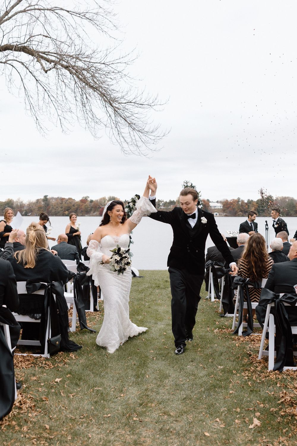 Outdoor wedding ceremony with guests seated on white chairs against natural landscape.