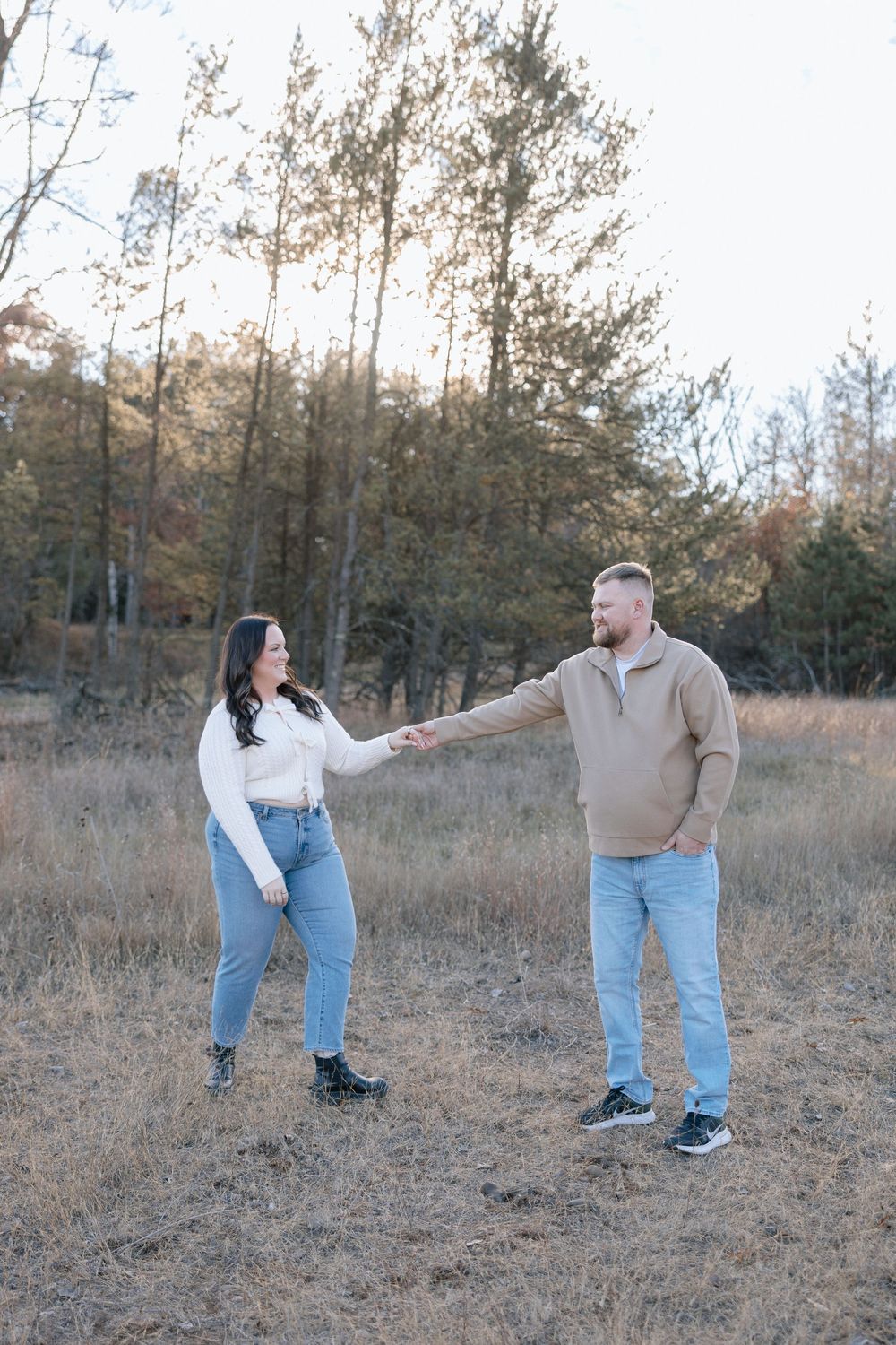 Couple in matching denim and light tops posing playfully in autumn field.