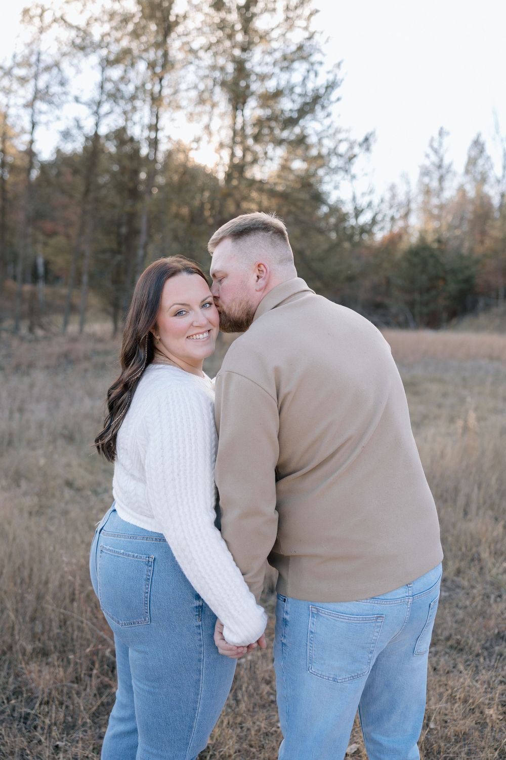 Couple in white sweater and beige top sharing intimate moment in fall field setting.