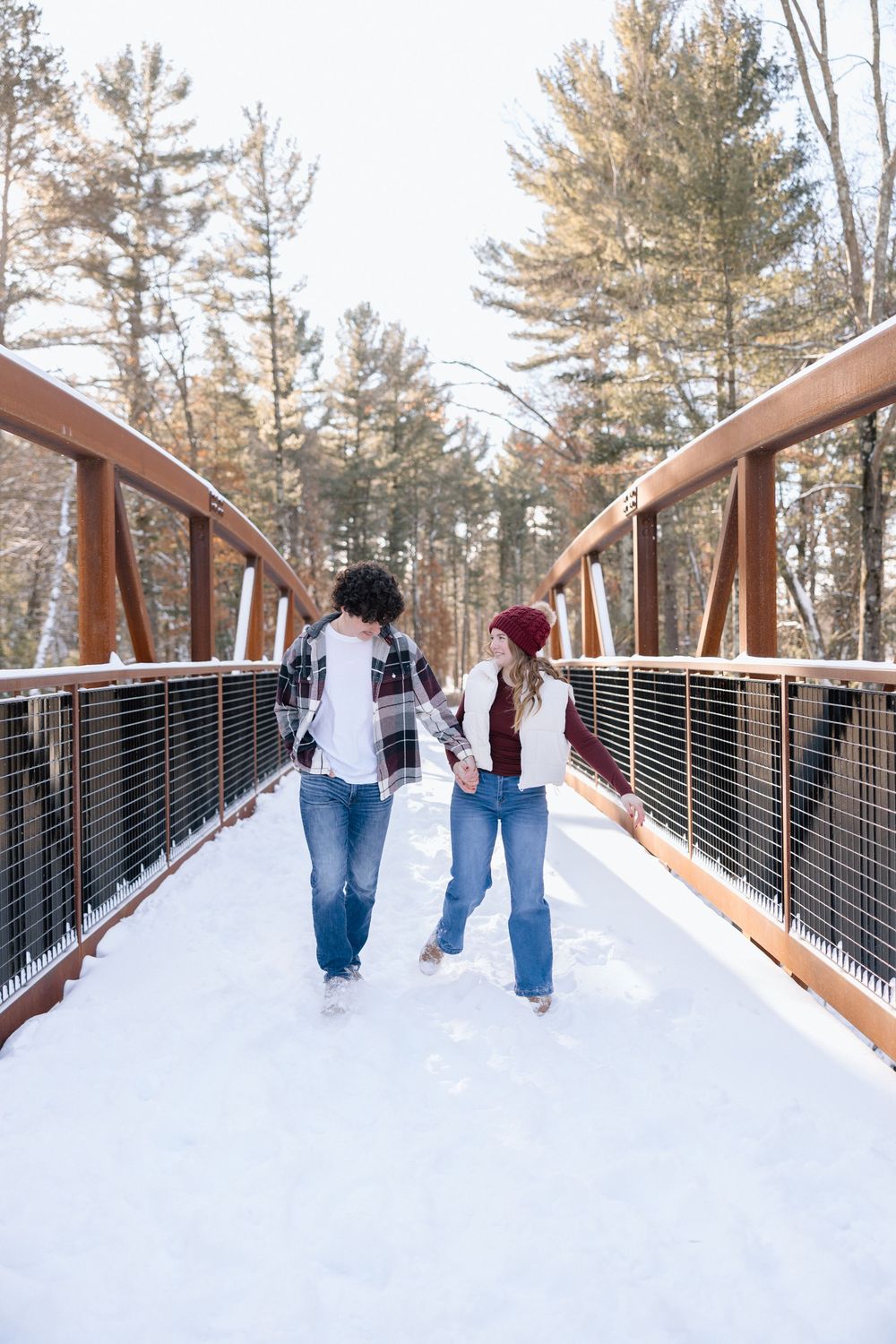 Sequence of couple walking along snow-covered wooden bridge in winter landscape.