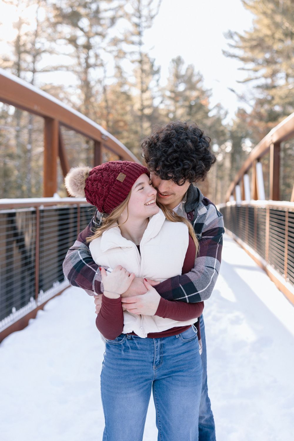 Romantic winter moments captured on snow-covered bridge with couple in burgundy and denim.