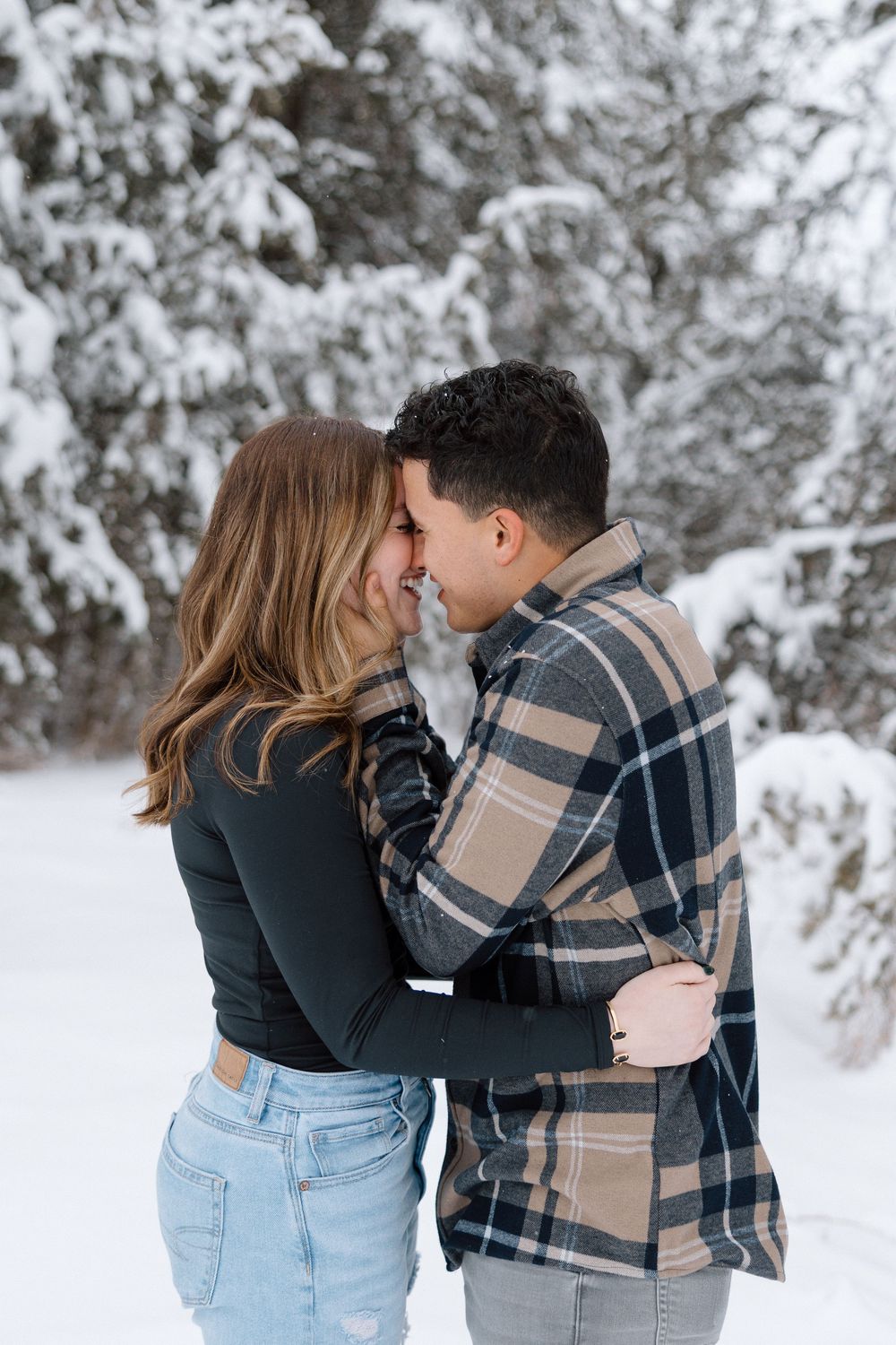 A couple shares intimate moments in a snowy winter forest setting.